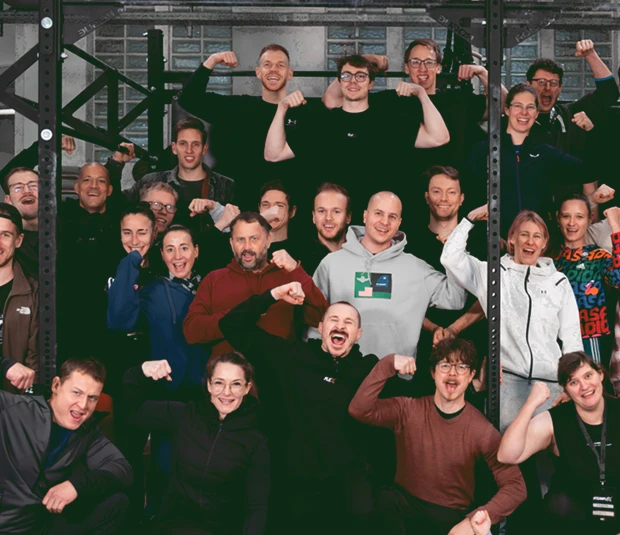 Gruppenfoto eines Trainingsteams in der Box, mehrere Personen posieren mit angespannten Armen vor einem Rig.