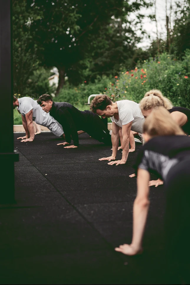 Gruppe trainiert draußen auf Gummiboden und macht Liegestütz- bzw. Plank-Übungen in einer Reihe.